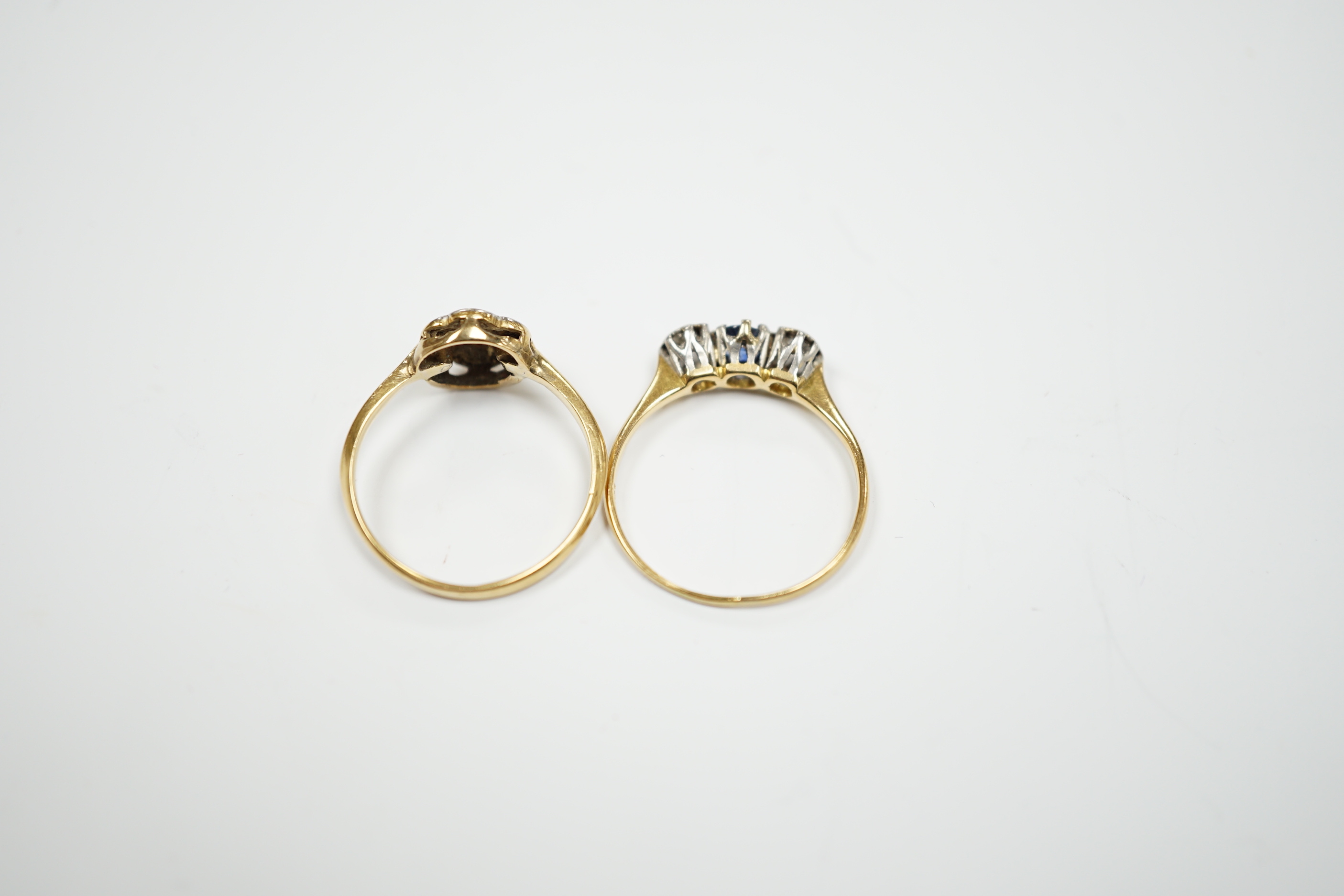 A 1920's 18ct, plat and diamond cluster set flower head ring, size M/N and a 18ct and plat. sapphire and diamond set three stone ring, size O/P, gross 3.9 grams.
